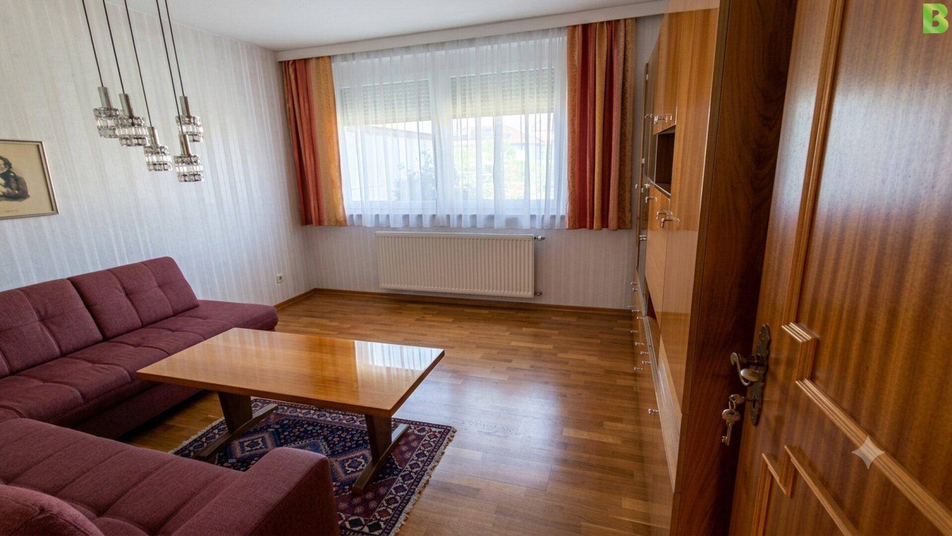 Wohnzimmer mit Parkettboden, rotem Ecksofa und großem Fenster.