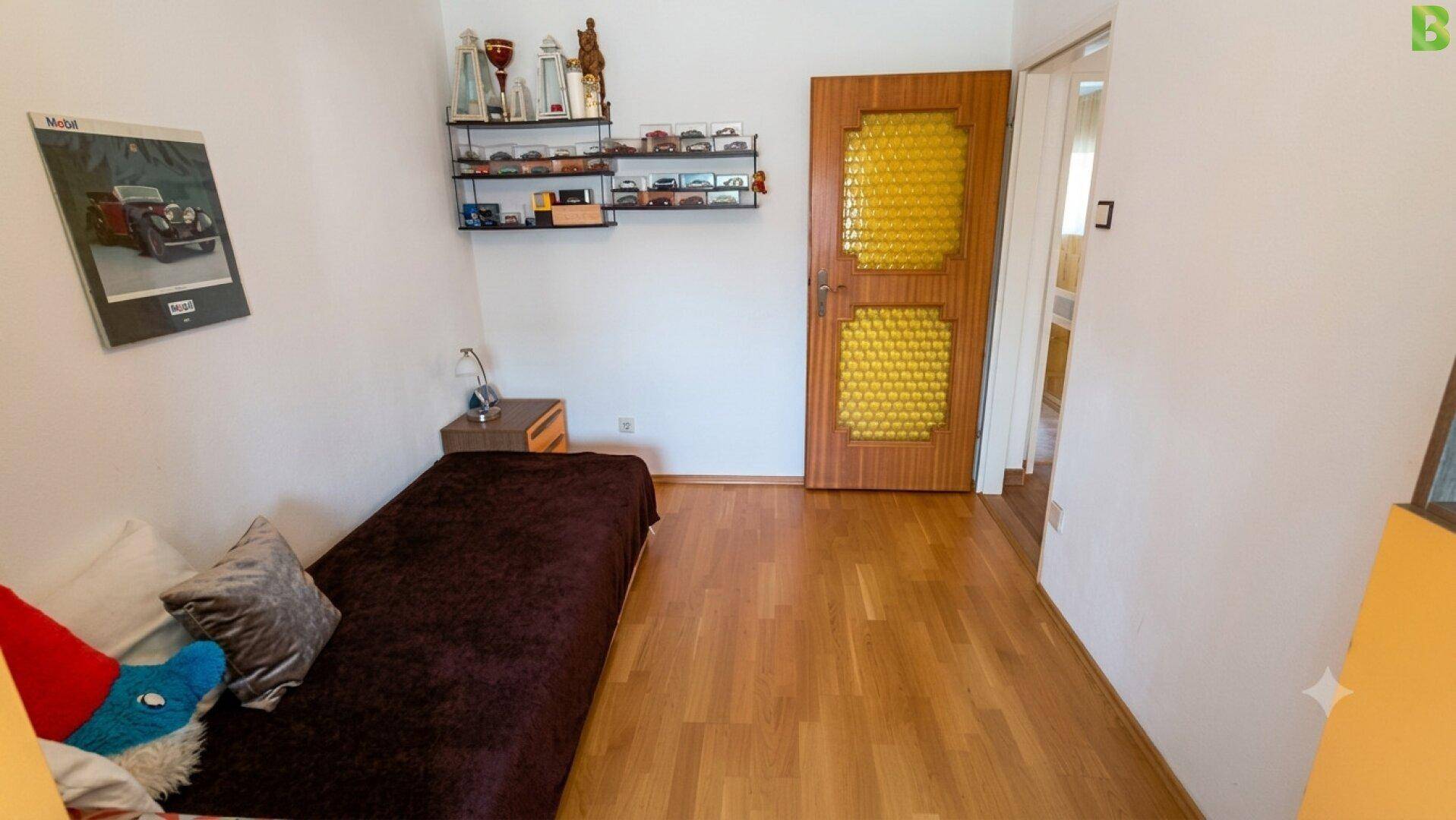 Kleines Schlafzimmer mit Einzelbett, Holzfußboden und dekorativer Tür.