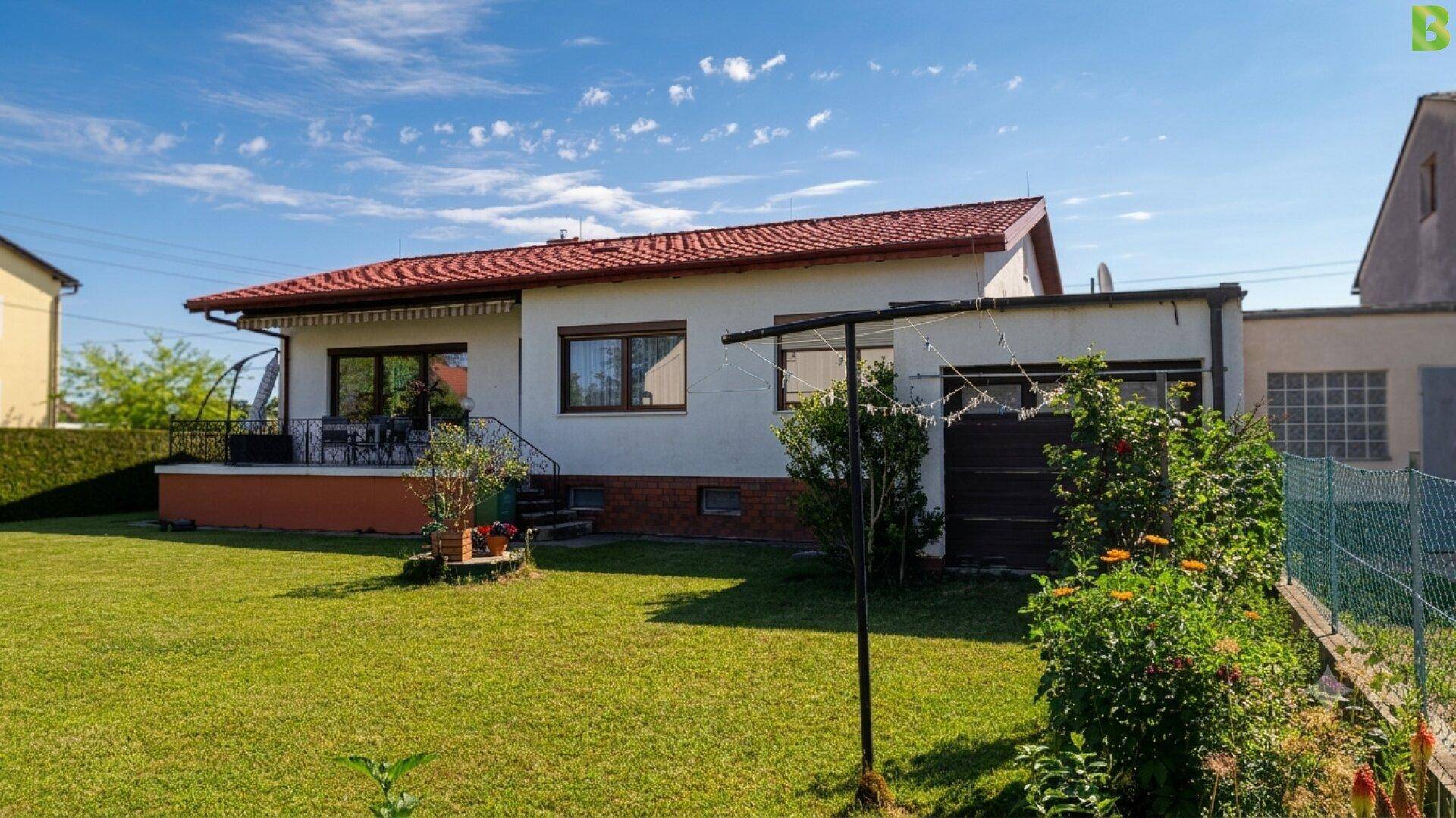 Rückansicht des Hauses mit großem Garten und Wäscheleine unter blauem Himmel.