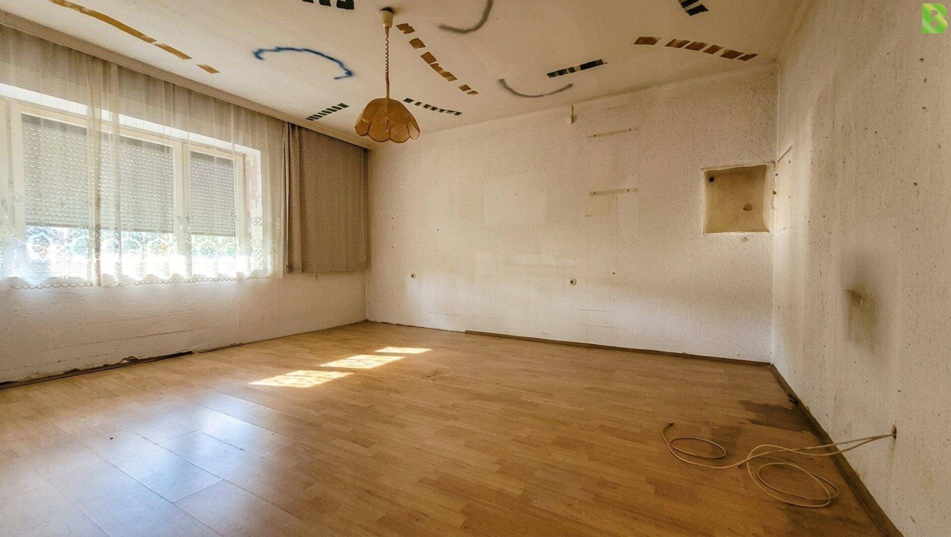 Helles, unmöbliertes Zimmer mit Laminatboden und Fenster, bereit für eine Renovierung.
