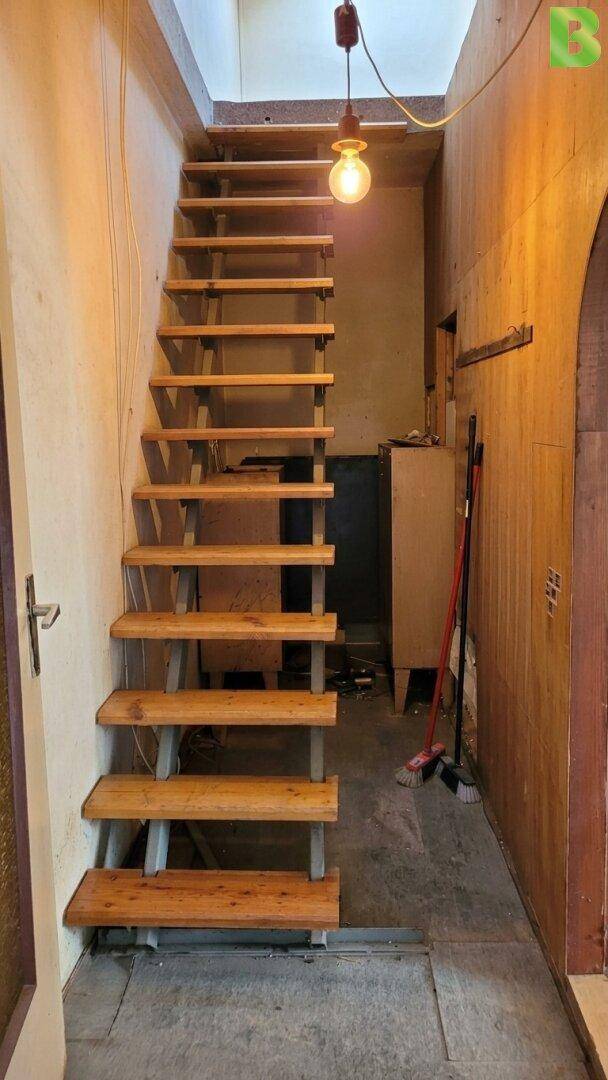 Schmale Holztreppe führt in die obere Etage, beleuchtet von einer einzelnen Glühbirne.