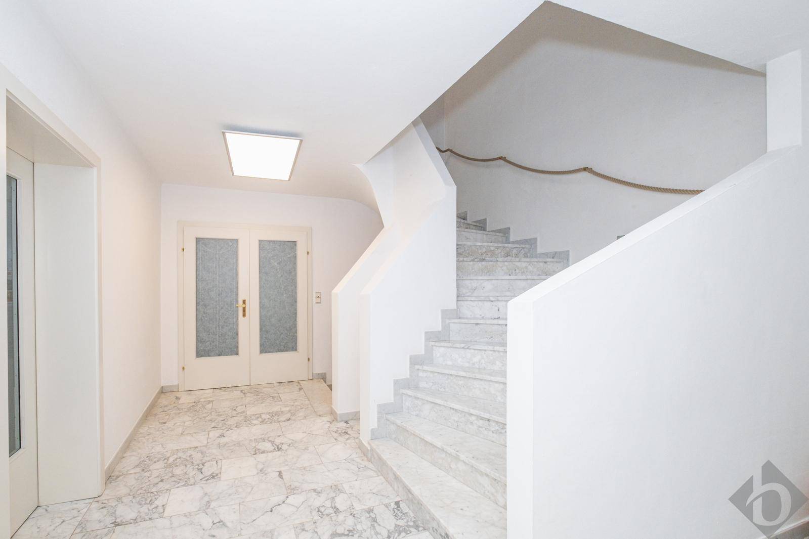 Heller Flur mit eleganter Marmortreppe und passendem Fliesenboden.