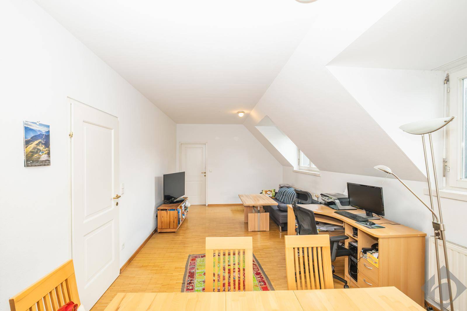 Geräumiger Wohnbereich mit Dachschrägen, Holzboden und viel Tageslicht durch die Dachfenster.