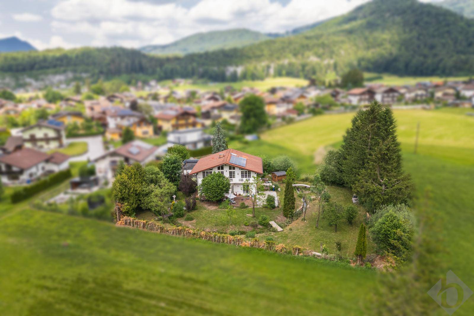 Miniaturansicht des Hauses mit Photovoltaikanlage, umgeben von grünen Feldern und Bergen.