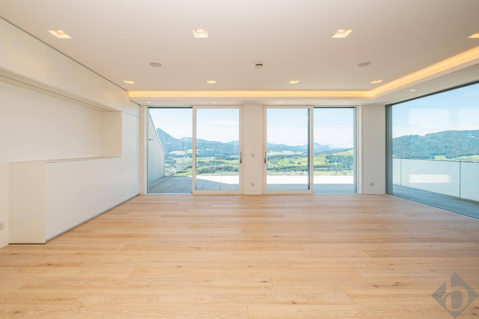 Geräumiges Wohnzimmer mit Holzboden, großen Schiebetüren und Panoramablick auf die Landschaft.