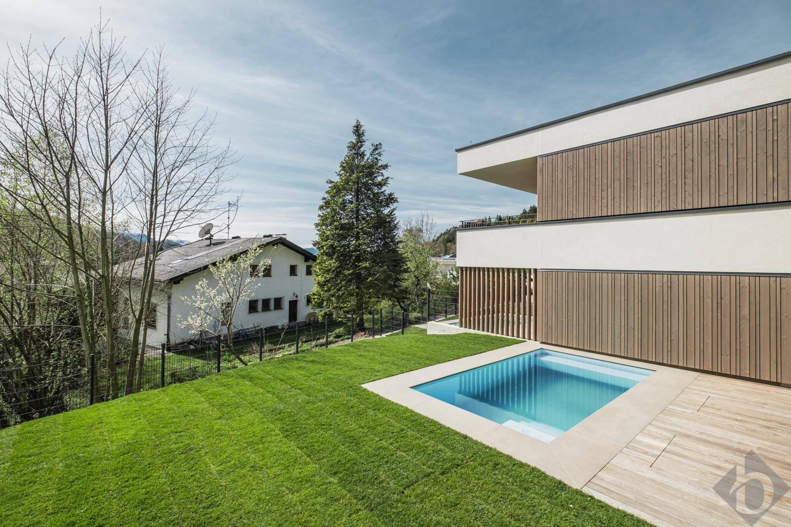 Seitliche Ansicht des modernen Gebäudes mit Pool und weitläufigem Rasenbereich.