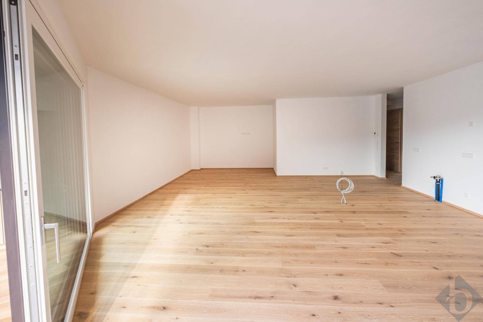 Geräumiger, heller Raum mit Holzboden und großen Fenstern, bereit zur Einrichtung.