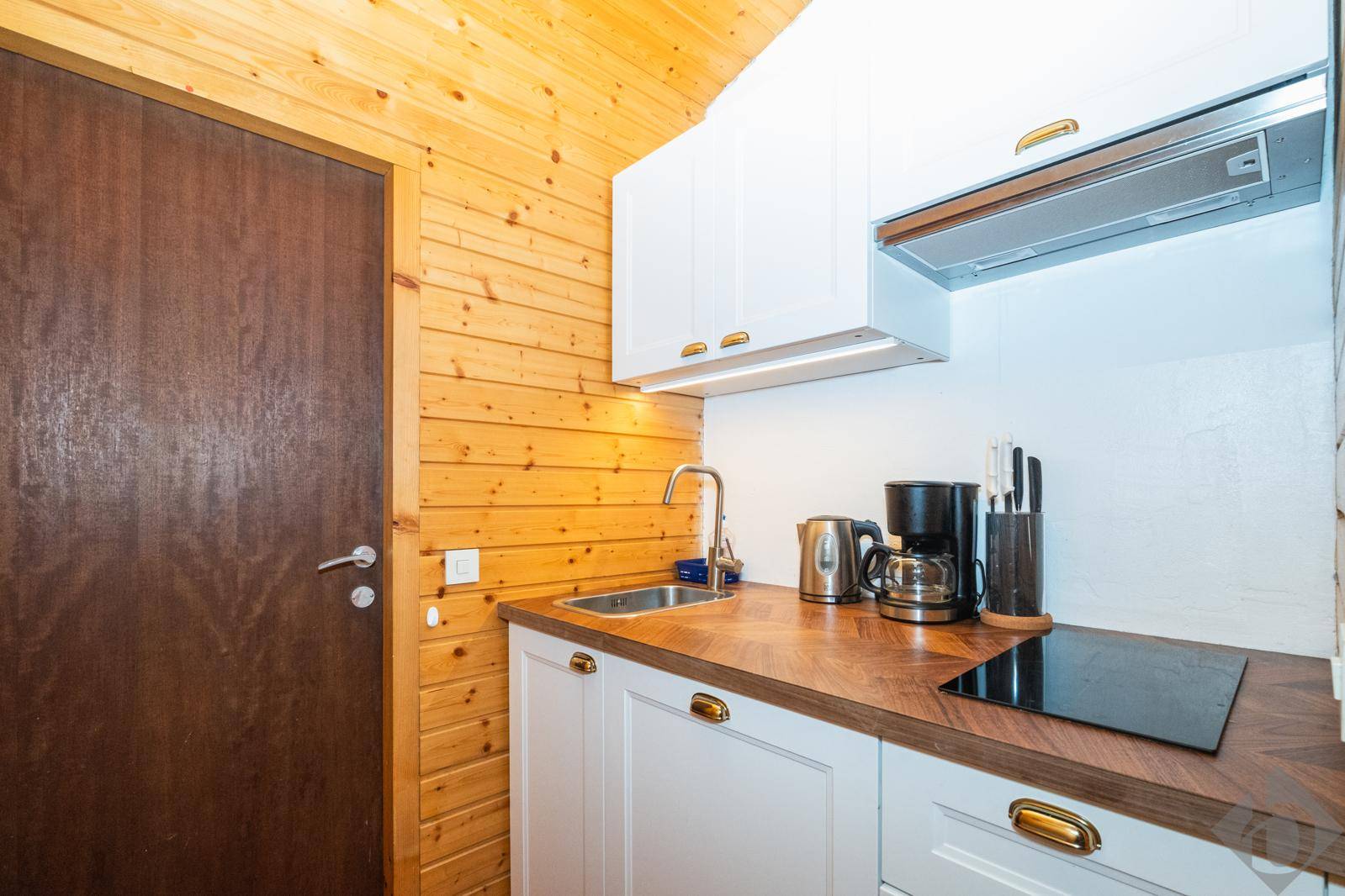 Kleine Küchenzeile mit Holzvertäfelung, weißen Schränken und integriertem Kochfeld.