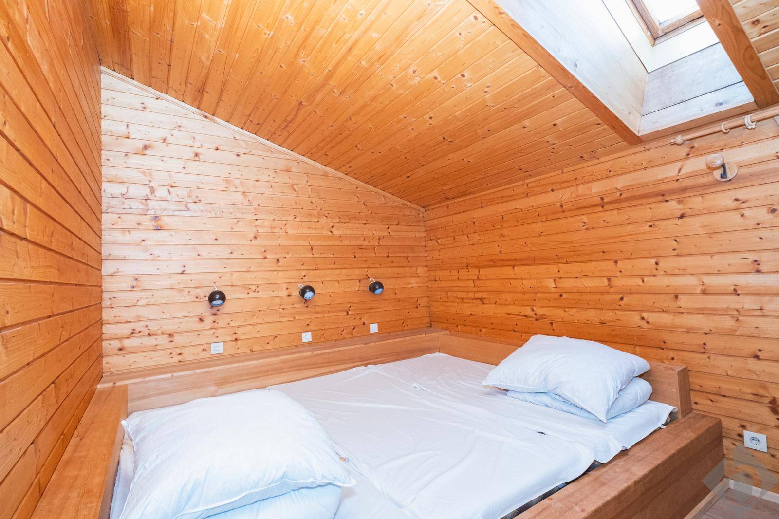 Schlafzimmer im Dachgeschoss mit Holzvertäfelung, Doppelbett und Dachfenster für natürliches Licht.