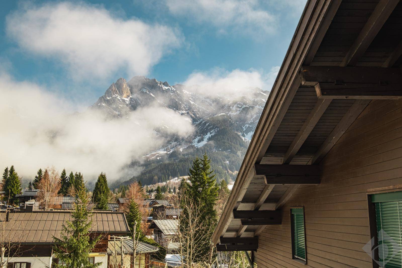 Malerischer Blick auf schneebedeckte Berge, umgeben von Wolken und einem traditionellen Hausdach.