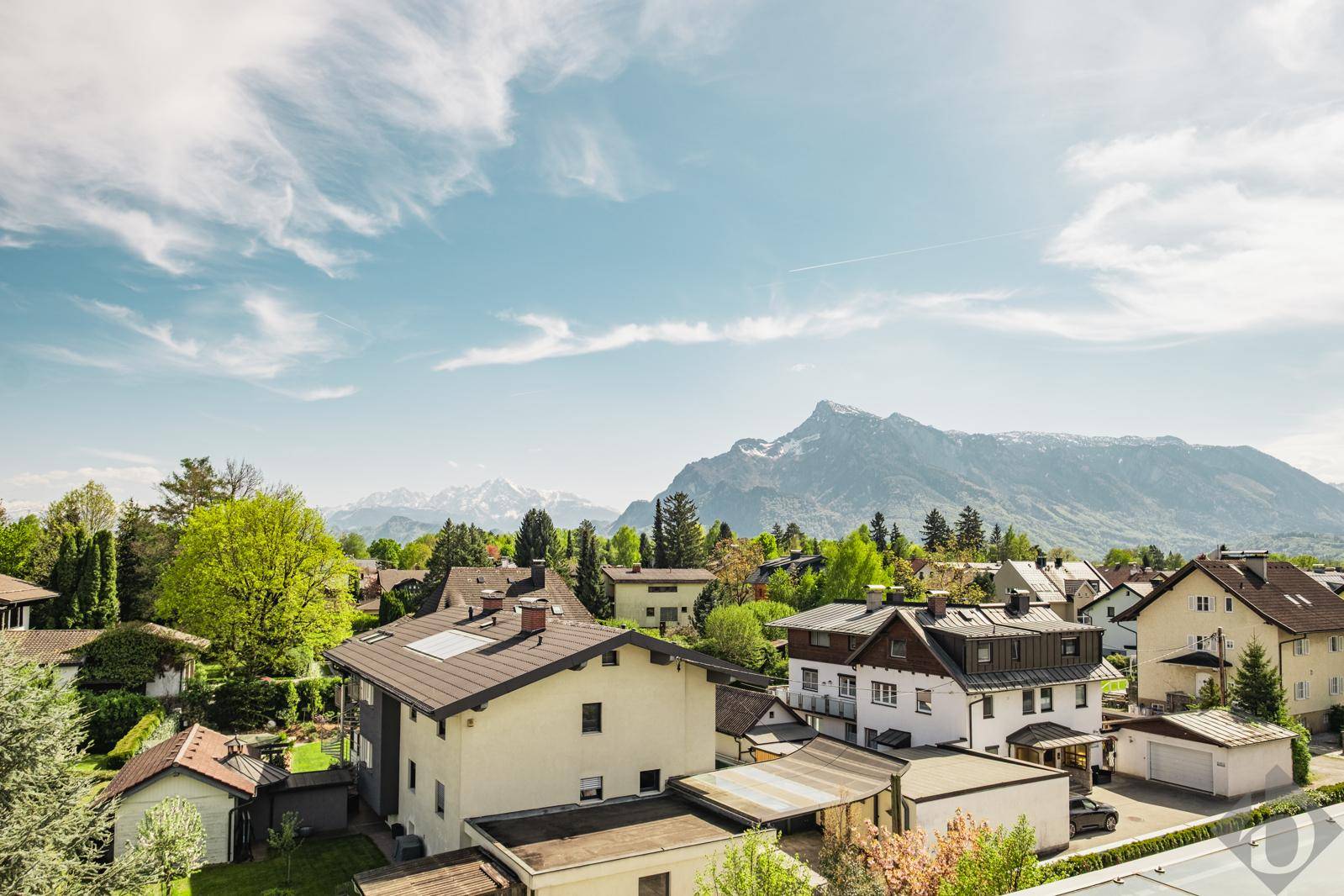 Panoramablick über eine Wohnsiedlung mit Bergen im Hintergrund unter blauem Himmel.
