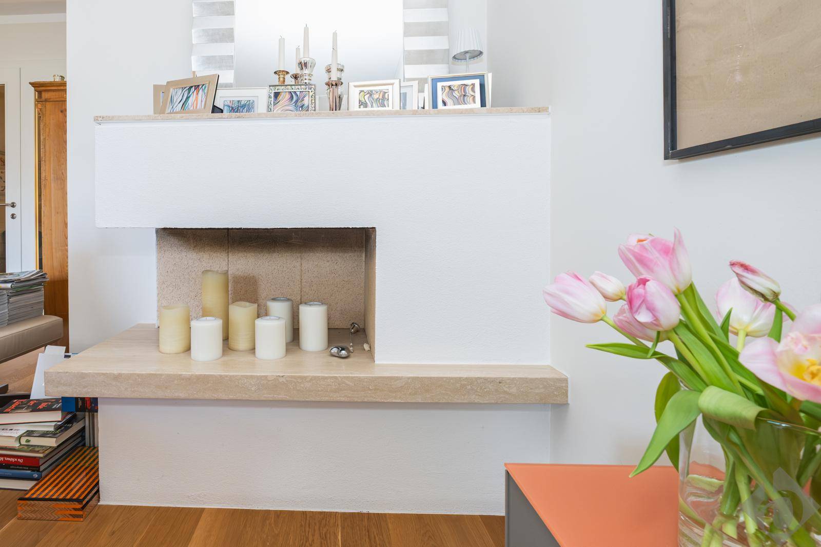 Moderner Kaminbereich im Wohnzimmer, dekoriert mit Kerzen und Blumen.