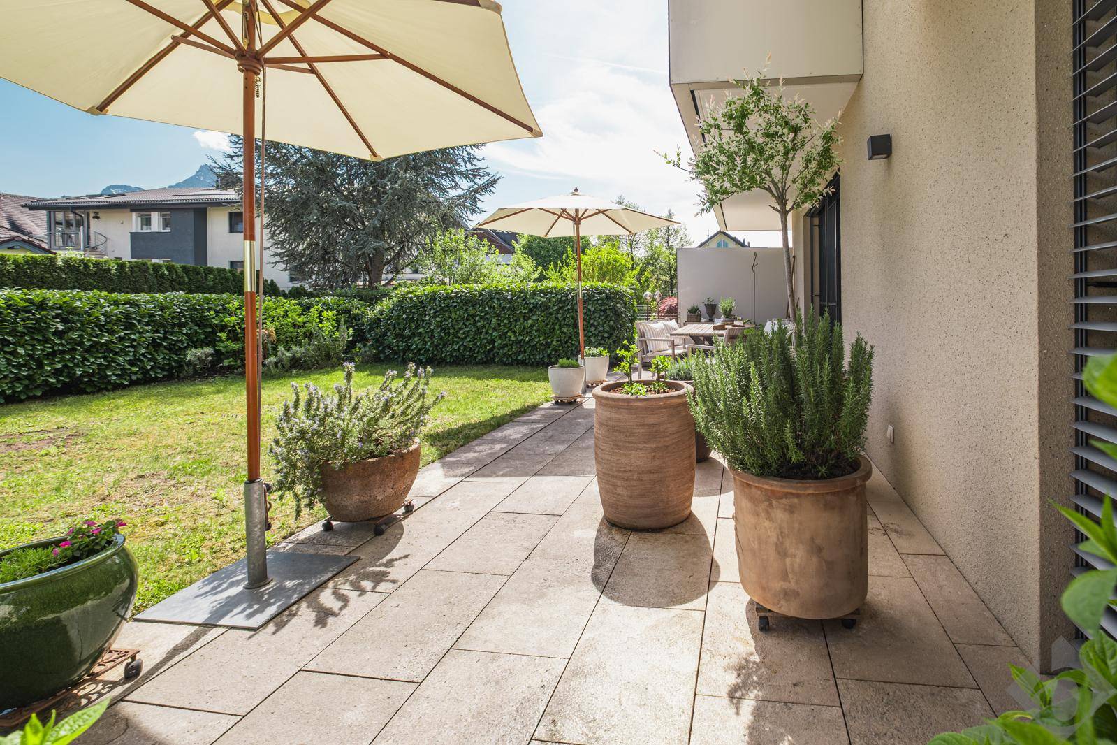 Große Steinterrasse mit Pflanzenkübeln und Blick auf den Garten.