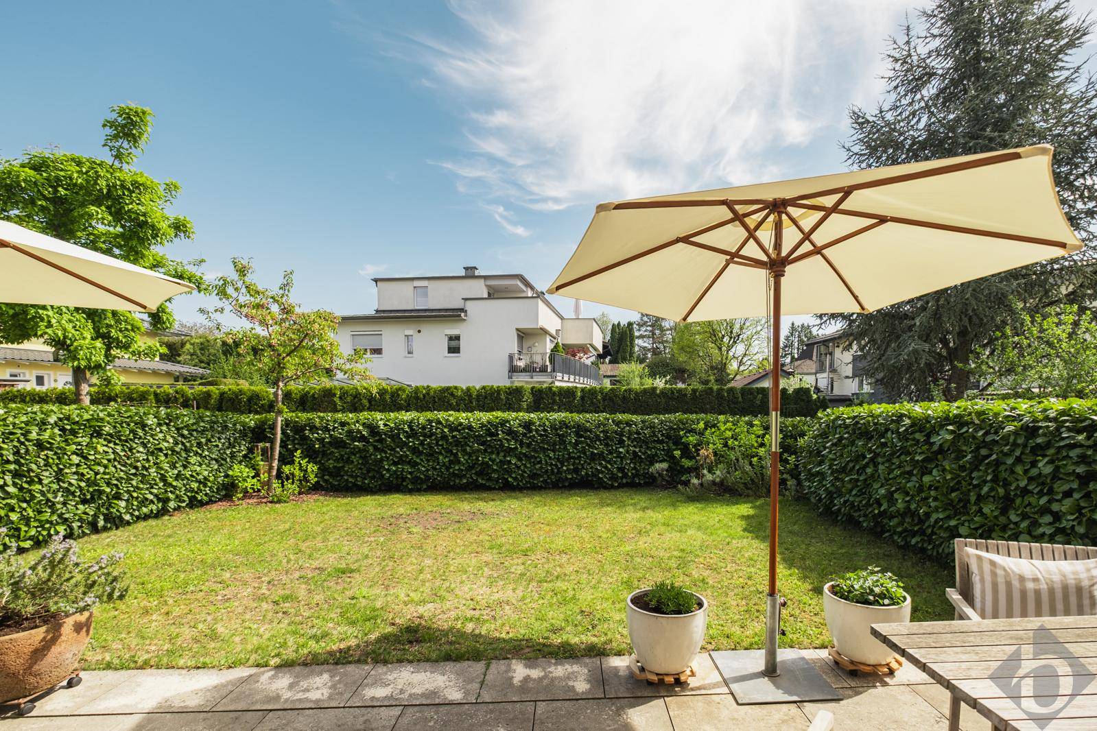 Gepflegter Garten mit Rasenfläche, Hecken und Sonnenschirm an einem sonnigen Tag.