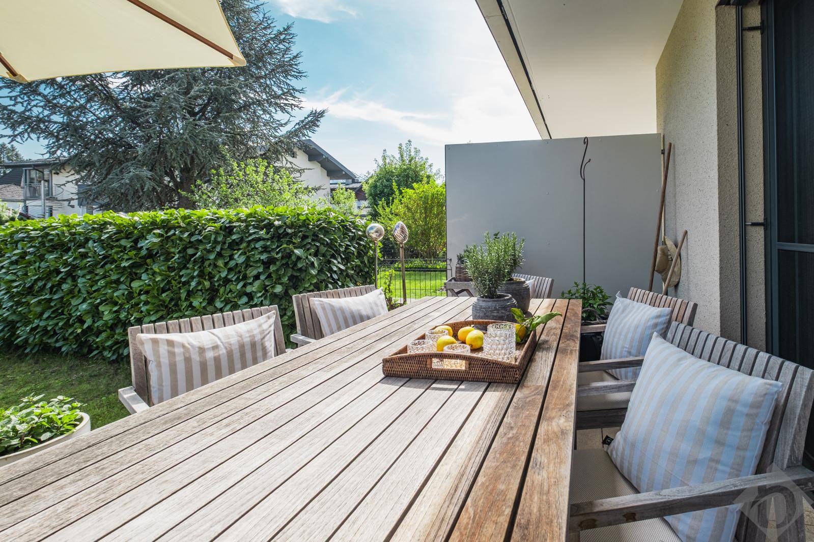 Gemütliche Terrasse mit Holztisch und Stühlen, umgeben von Grün und mit Blick in den Garten.