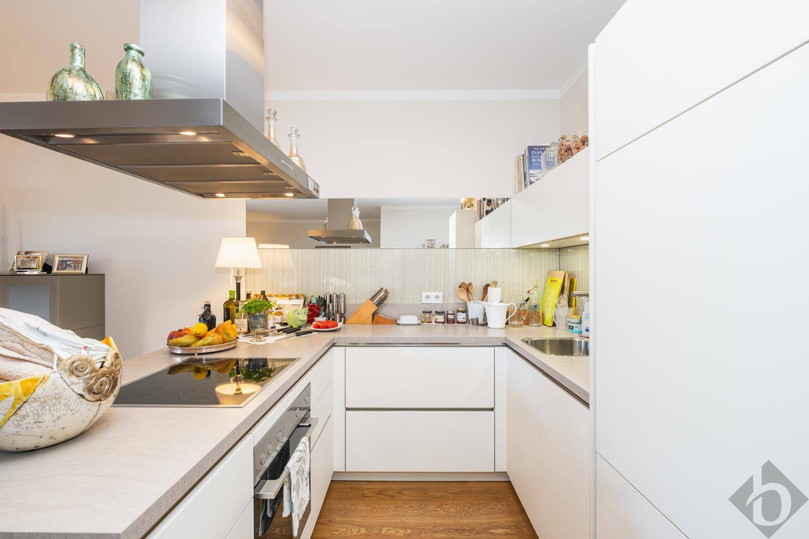 Moderne Einbauküche mit weißen Fronten, Induktionskochfeld und Dunstabzugshaube.