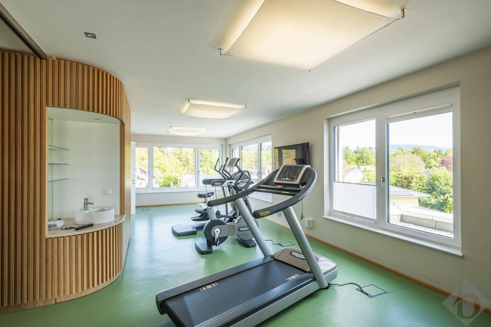 Heller Fitnessraum mit modernen Trainingsgeräten und großen Fenstern.