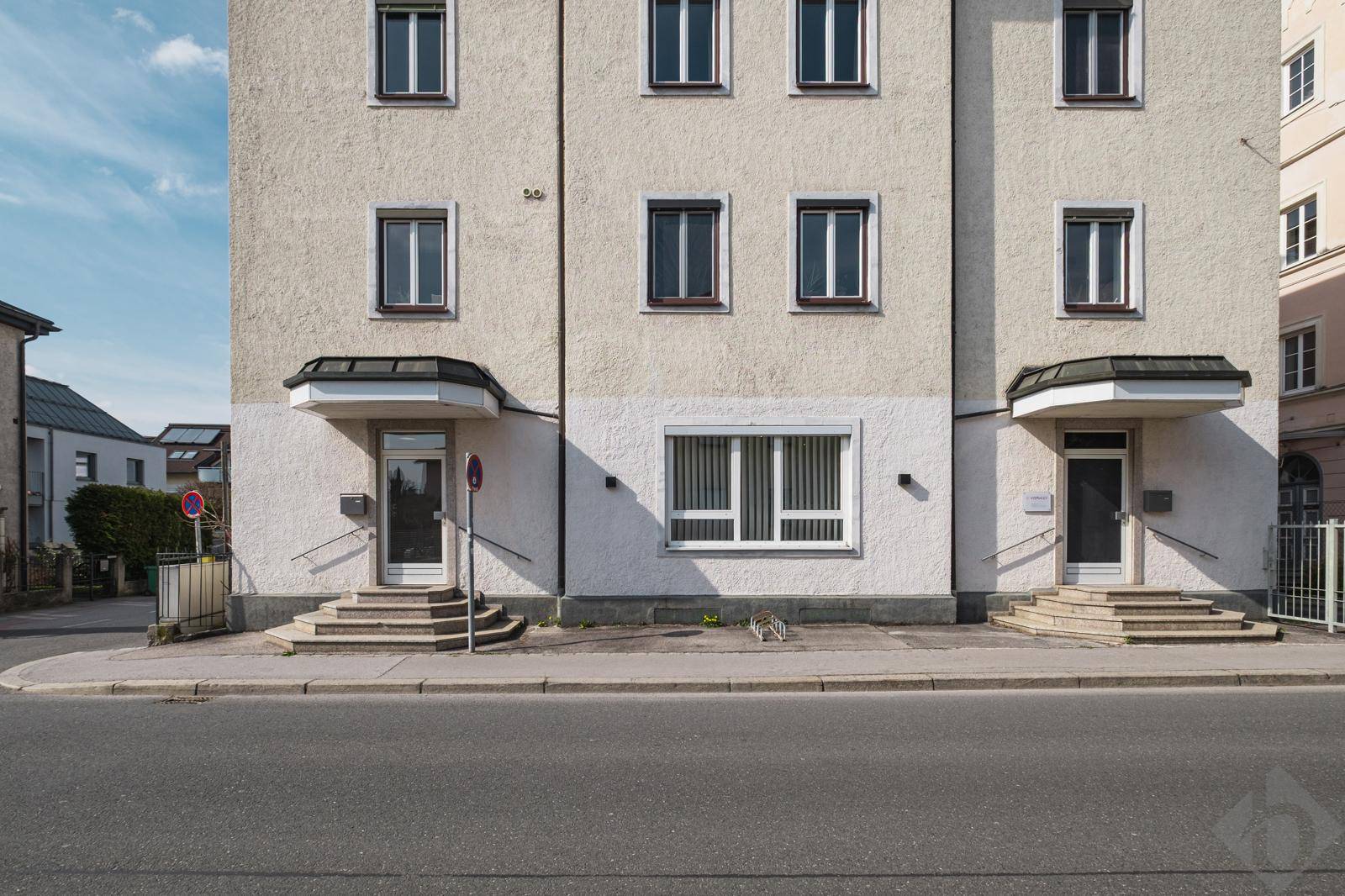 Fassade eines Mehrfamilienhauses mit mehreren Fenstern und zwei Eingangstüren.
