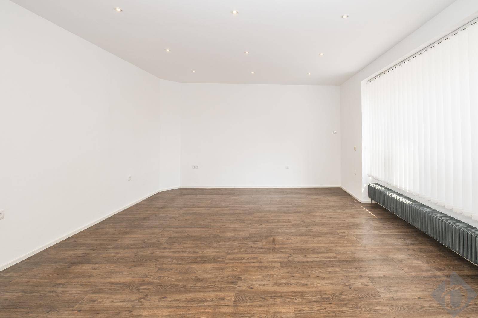 Großer, heller Raum mit Laminatboden, Einbaustrahlern und einem breiten Fenster mit Jalousien.