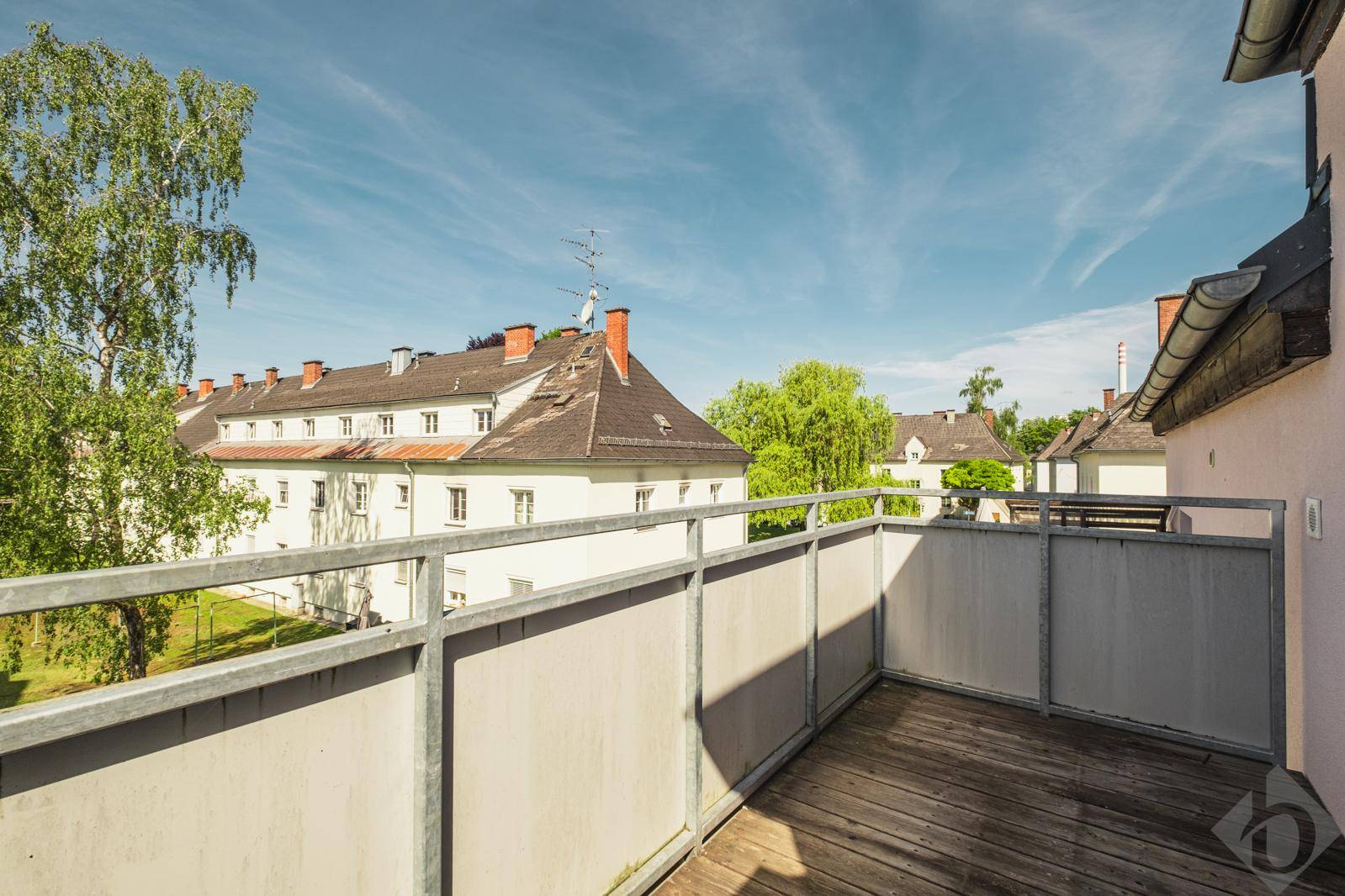 Geräumiger Balkon mit Holzboden und Blick auf die umliegenden Gebäude und Bäume.