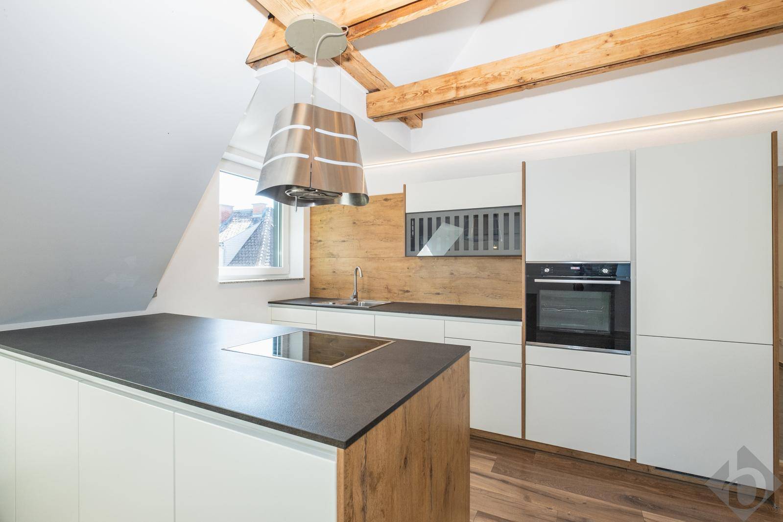 Moderne Einbauküche mit Kochinsel, Induktionskochfeld und Holzakzenten unter Dachschräge.