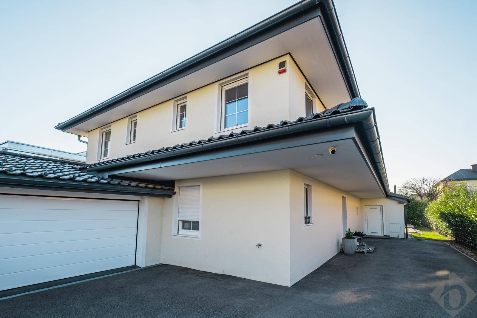 Seitenansicht des modernen Hauses mit integrierter Garage und gepflegter Zufahrt unter klarem Himmel.