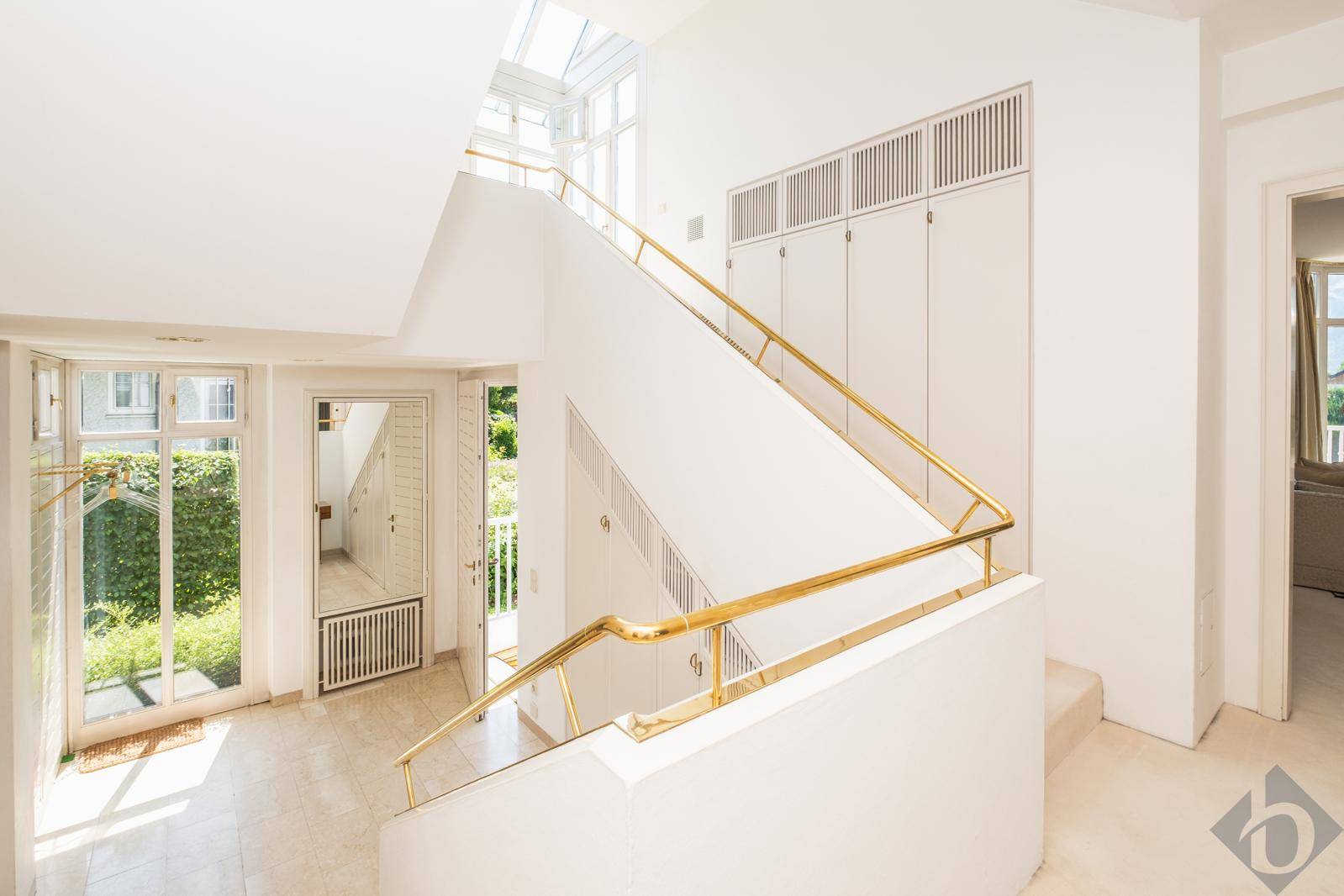 Heller Eingangsbereich mit eleganter Treppe, goldenen Geländern und Oberlicht für viel Tageslicht.