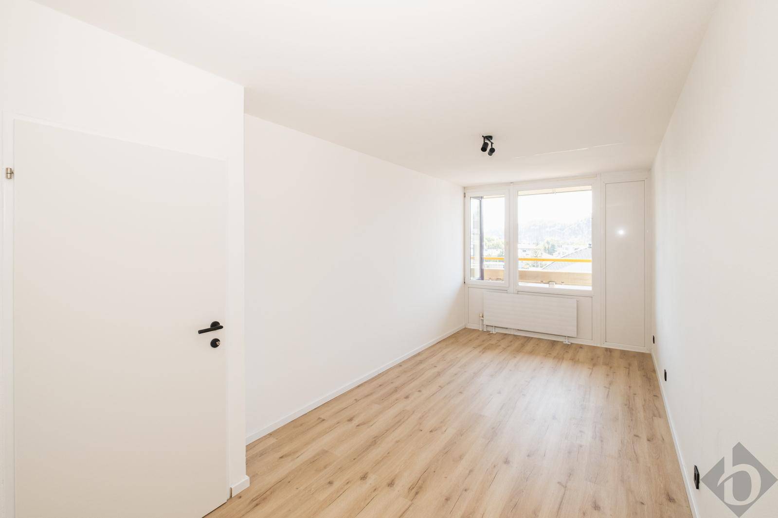 Helles Schlafzimmer mit Holzfußboden, großem Fenster und Zugang zu einem Balkon mit Fernblick.