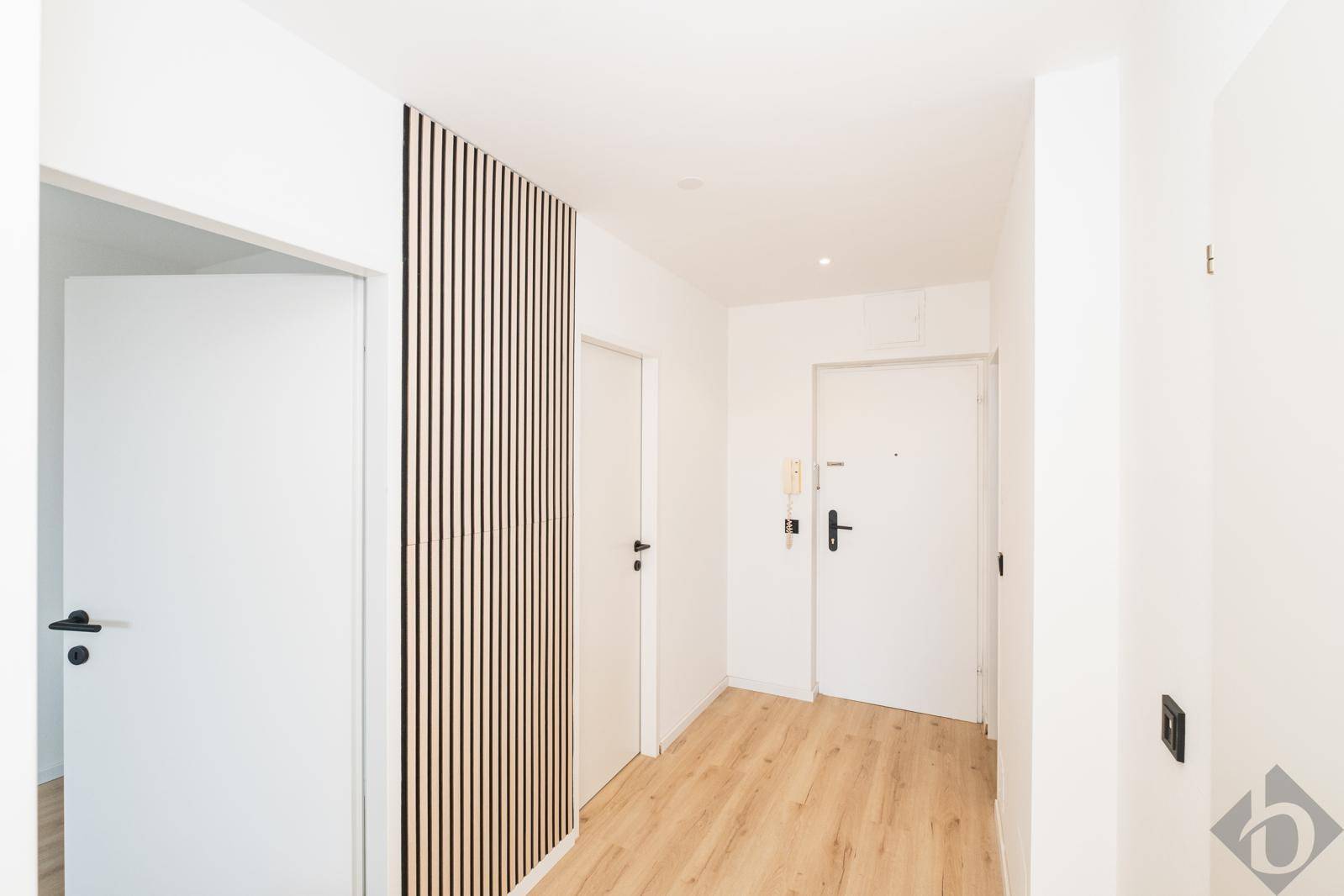 Heller Flur mit modernem Holzlatten-Design an der Wand, weißen Türen und hellem Holzfußboden.