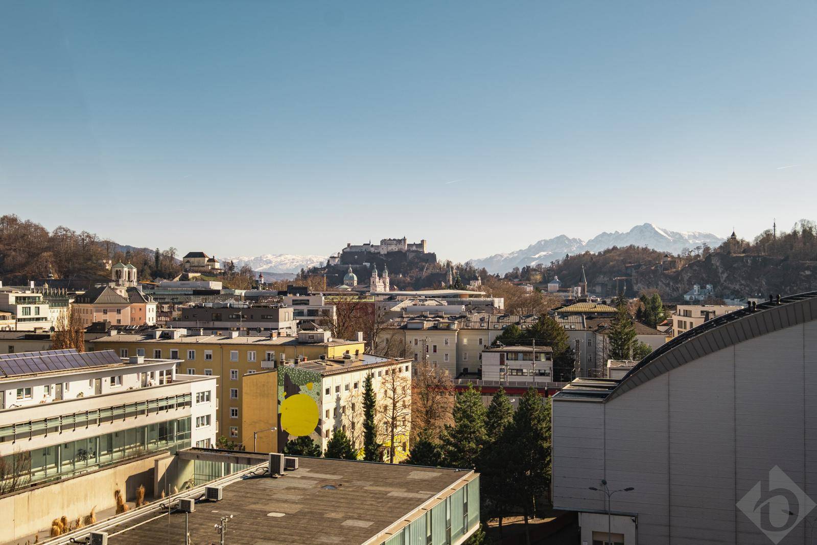 Panoramablick über die Stadt mit historischen Gebäuden, Bergen und einer Festung im Hintergrund.