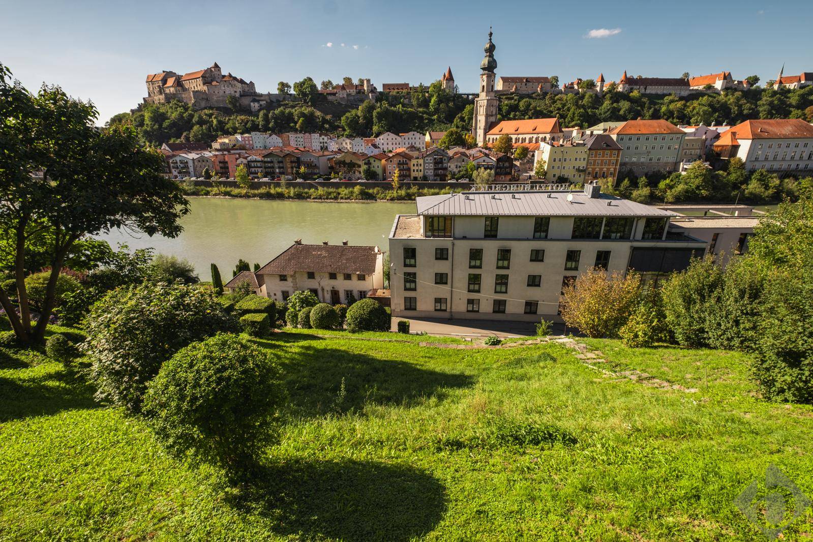 Blick von einem grünen Hang auf die Stadt, den Fluss und ein modernes Gebäude im Vordergrund.