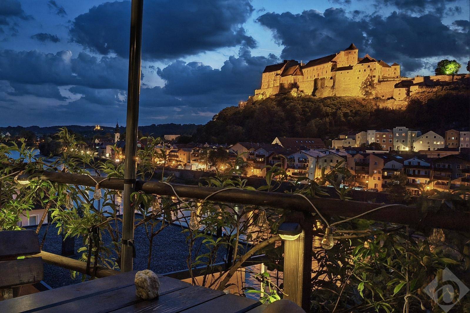 Abendlicher Blick von einem Balkon auf die beleuchtete Stadt, den Fluss und die majestätische Burg.