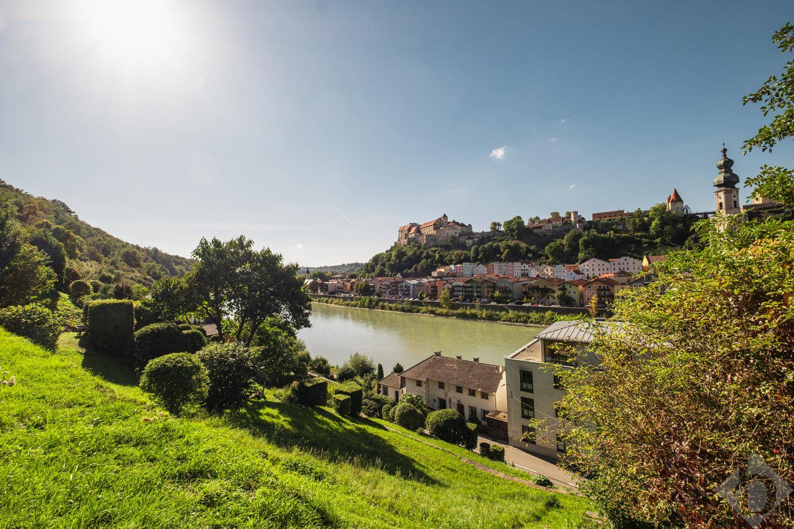 Sonniger Ausblick von einem grünen Hügel auf die Stadt, den Fluss und die historische Burg.
