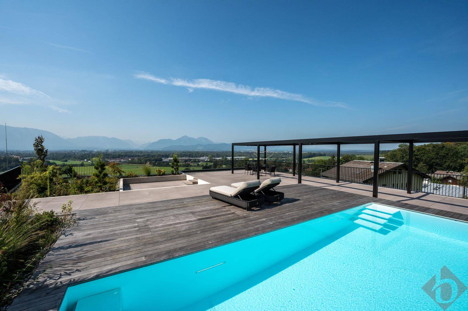 Weitläufige Poolterrasse mit Holzdeck, Liegeflächen und beeindruckendem Bergblick unter blauem Himmel.
