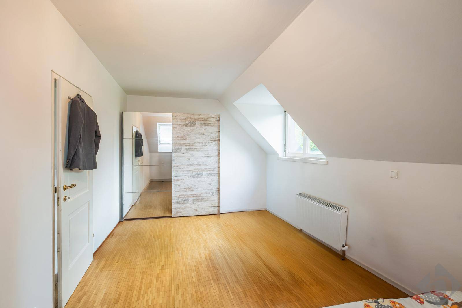 Schlafzimmer mit Holzboden, Dachschräge und einem großen Spiegelschrank für viel Stauraum.