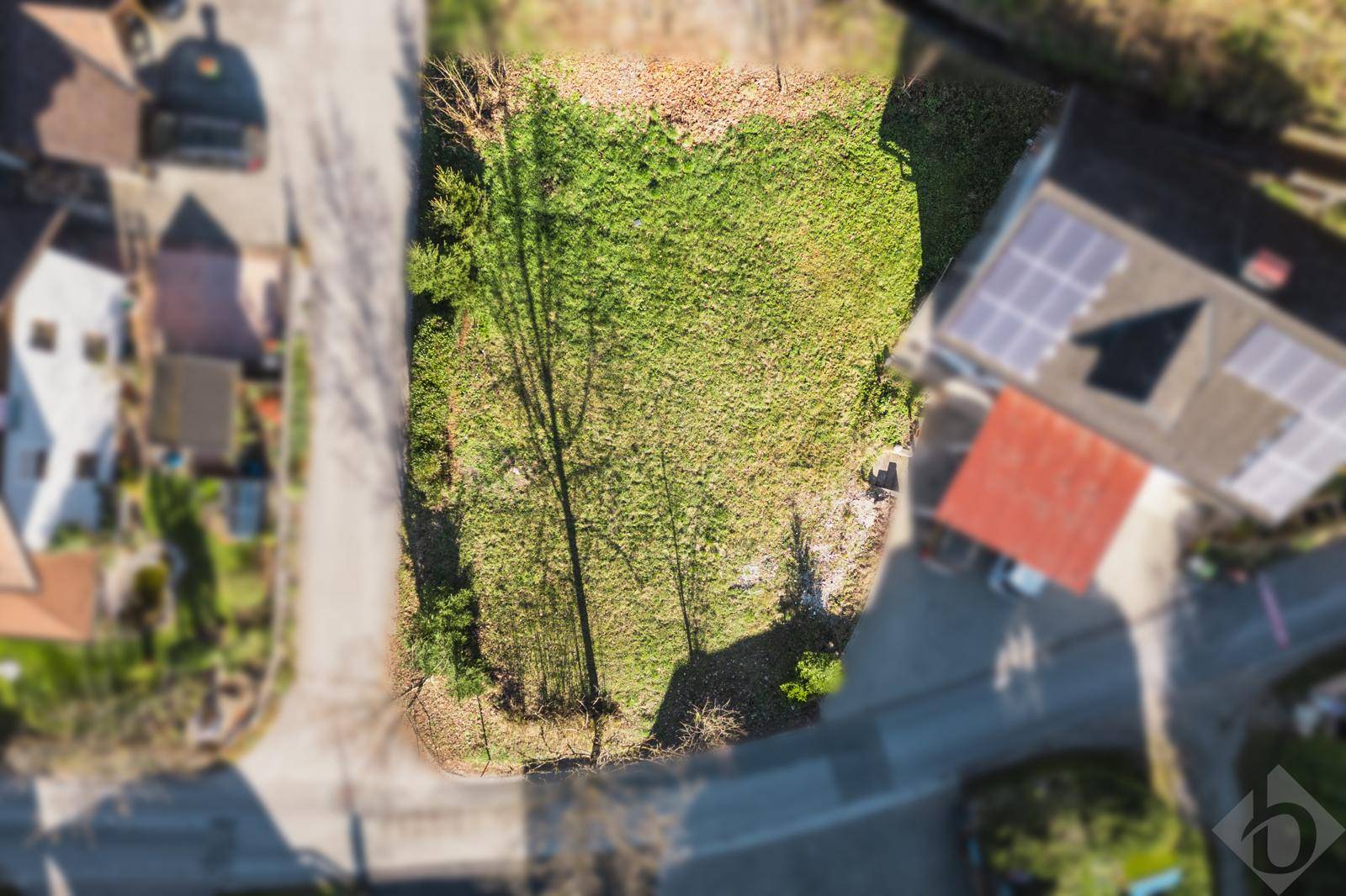Luftaufnahme eines Grundstücks mit Rasen und Bäumen, umgeben von Wohnbebauung und Straßen.