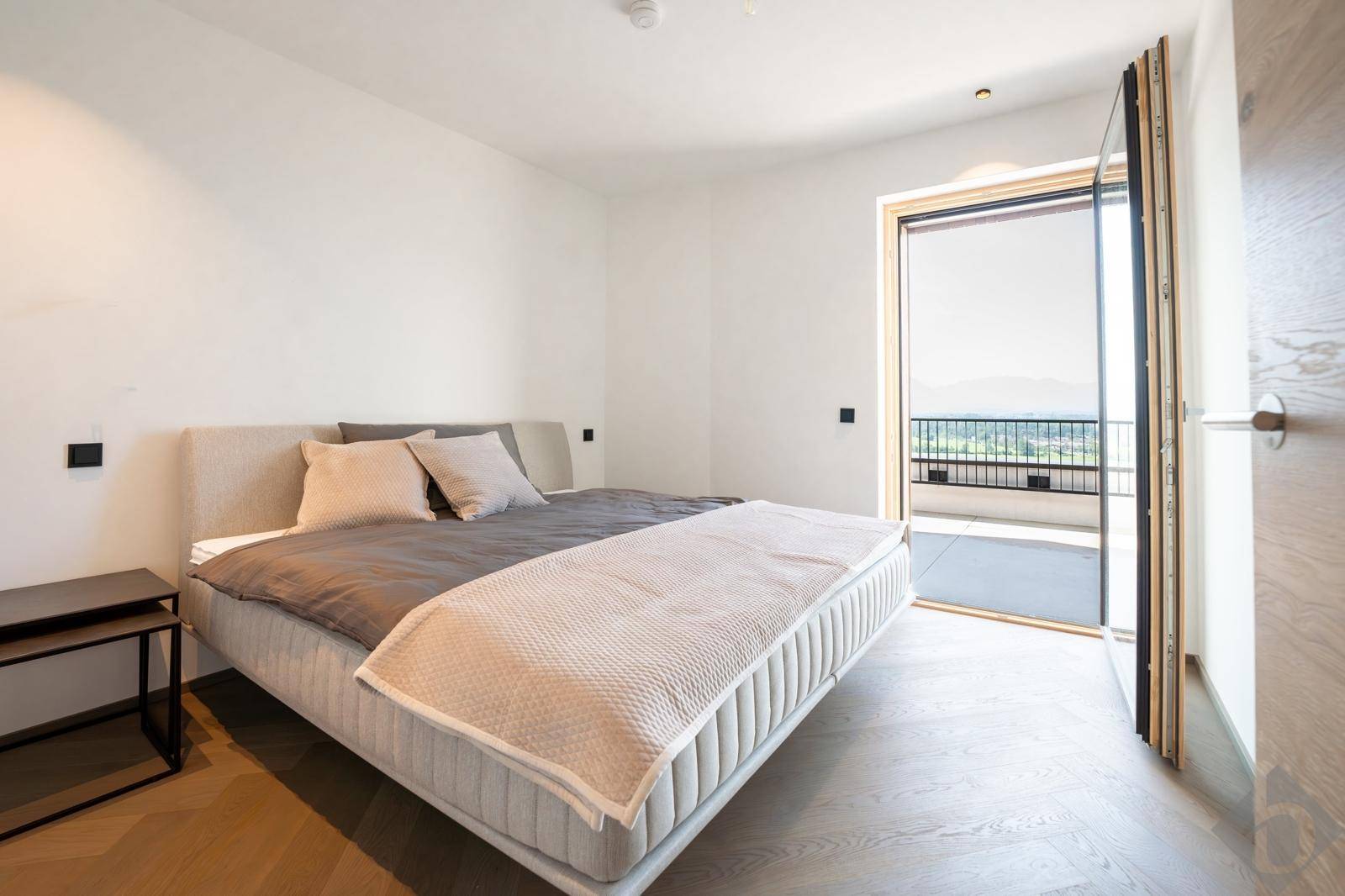 Helles Schlafzimmer mit modernem Bett, Holzboden und direktem Zugang zu einem Balkon mit Weitblick.