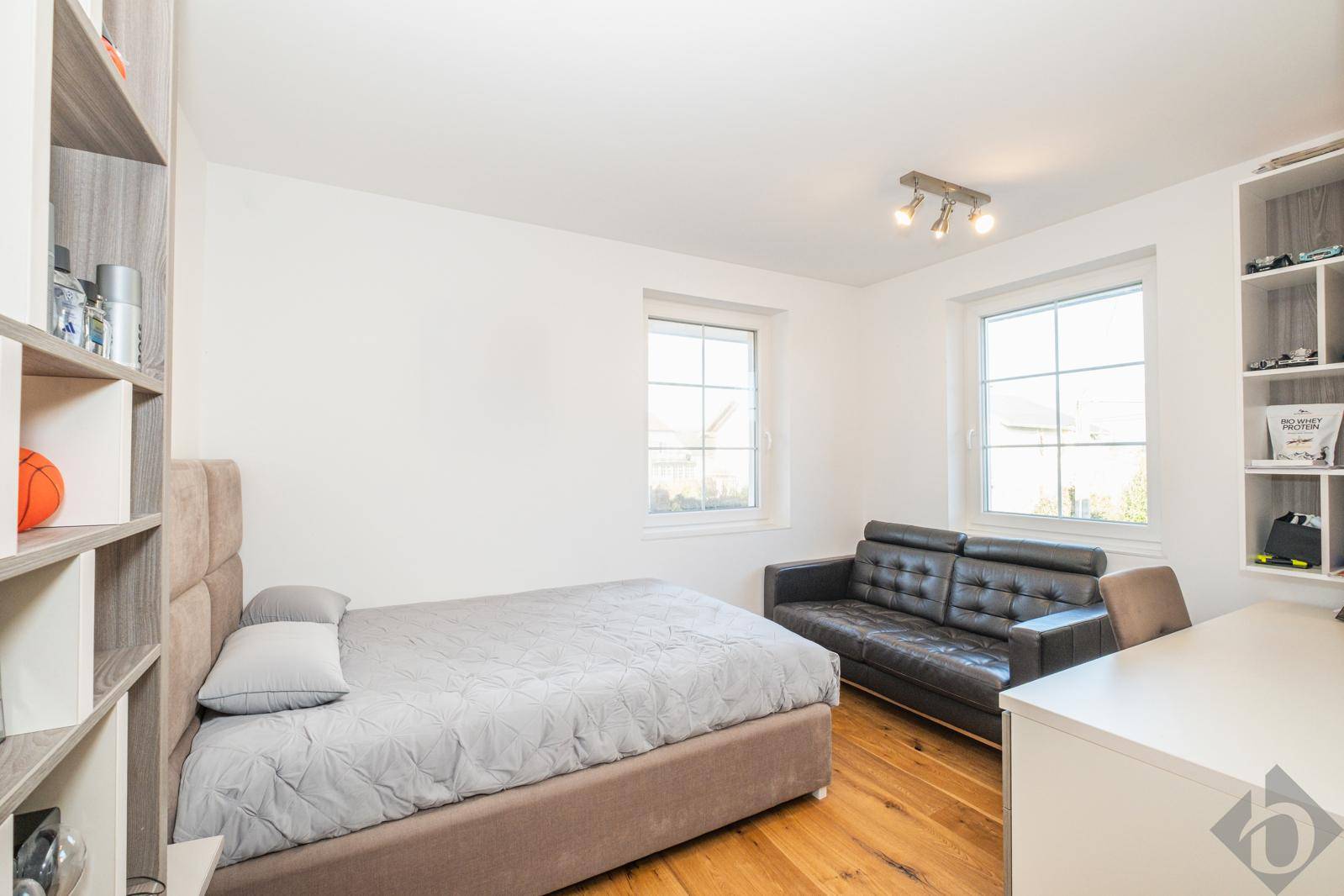 Gemütliches Schlafzimmer mit Holzboden, zwei Fenstern und einem Sofa.