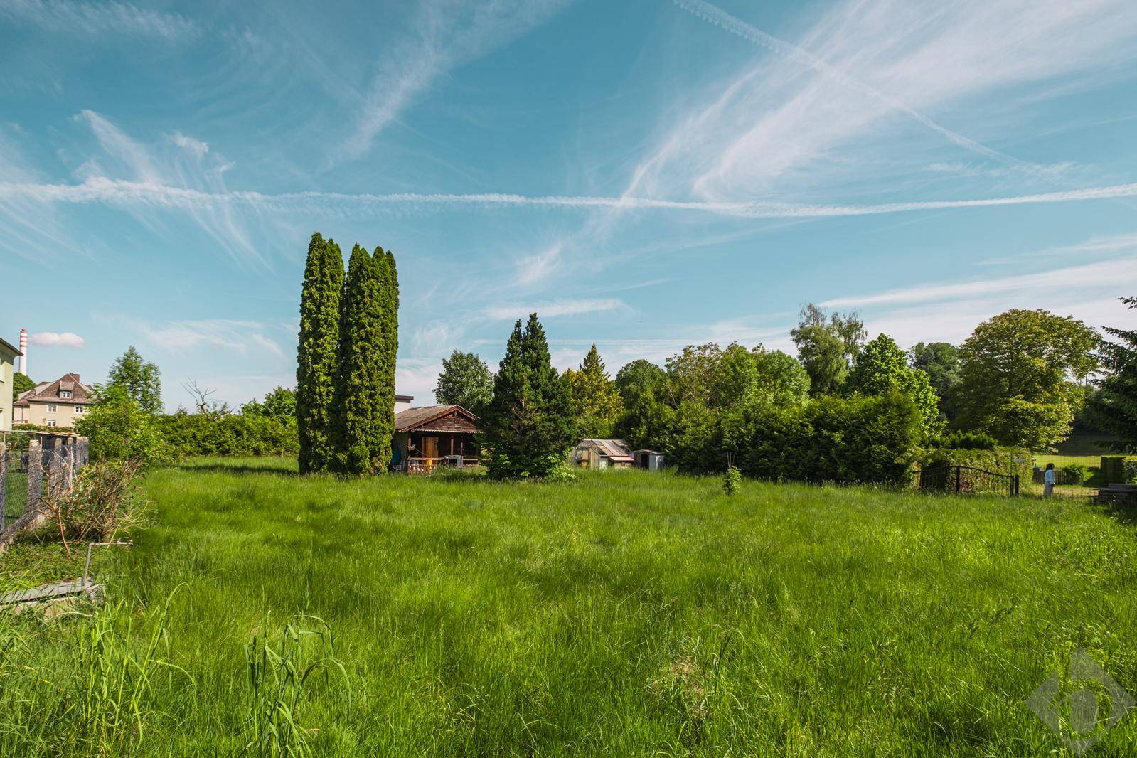 Großes, grünes Grundstück mit einem kleinen Holzhaus im Hintergrund und viel Natur.