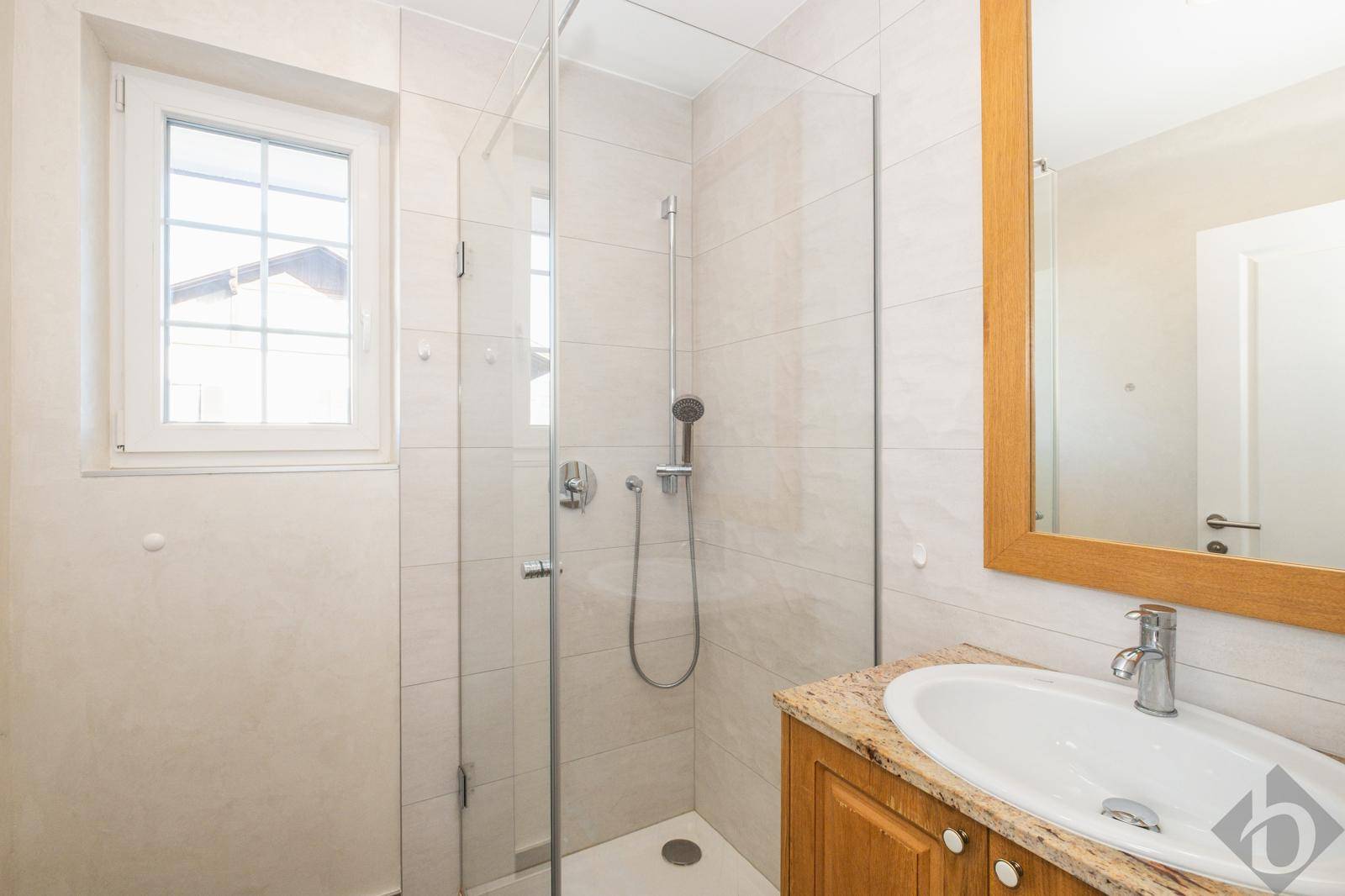 Modernes Badezimmer mit Dusche, Fenster und Waschtisch mit Granitplatte.