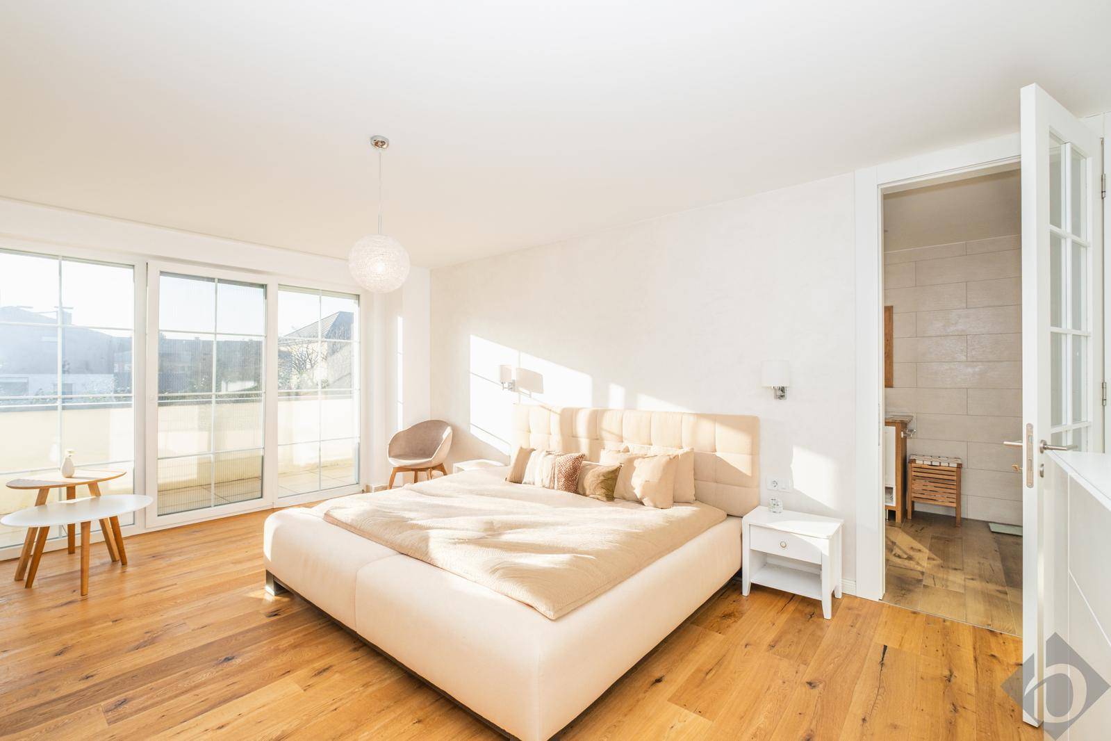 Helles Schlafzimmer mit großem Bett, Holzboden und Zugang zu einem Balkon oder Terrasse.