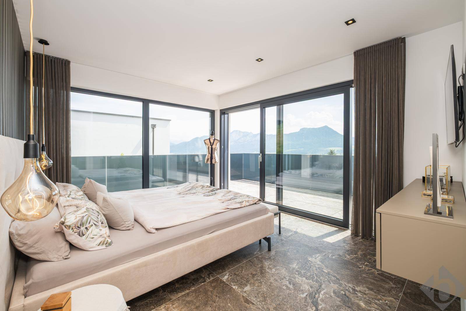 Helles Schlafzimmer mit großem Bett, modernen Leuchten und Panoramafenstern mit Bergblick.
