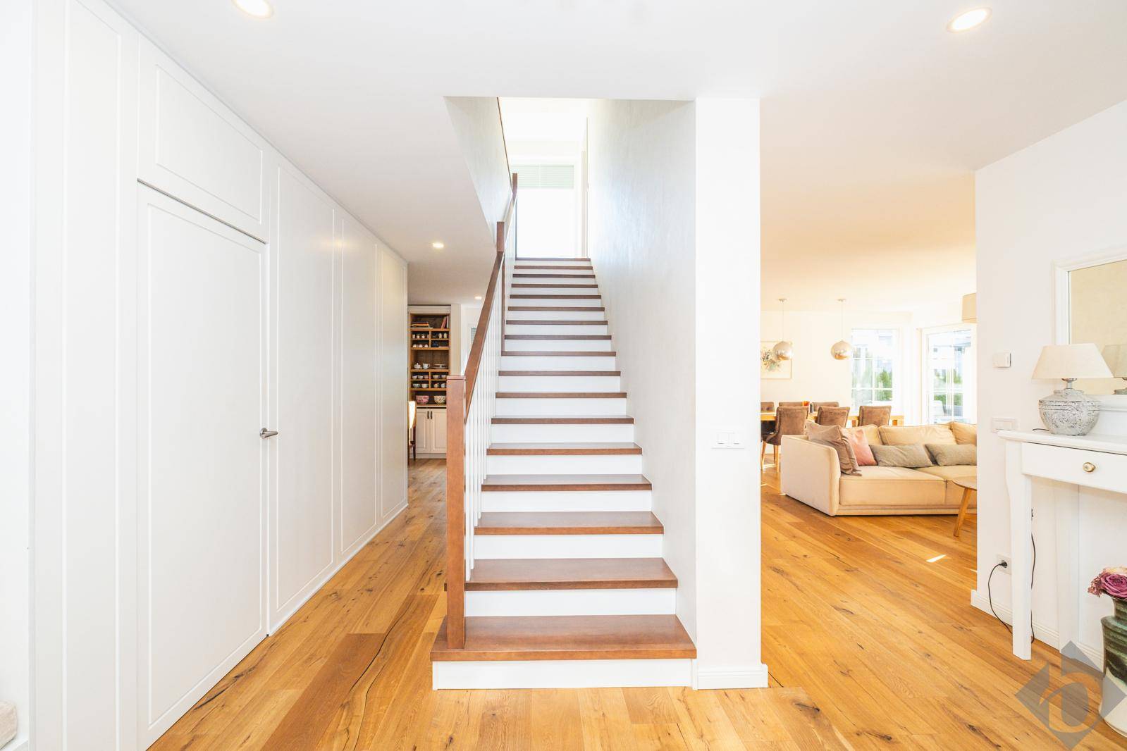 Heller Flur mit Holztreppe, integrierten Schränken und Eichenparkettboden.