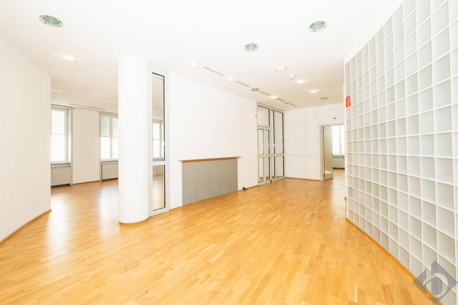 Heller, offener Bürobereich mit Holzfußboden, Säulen und einer dekorativen Glasbausteinwand.
