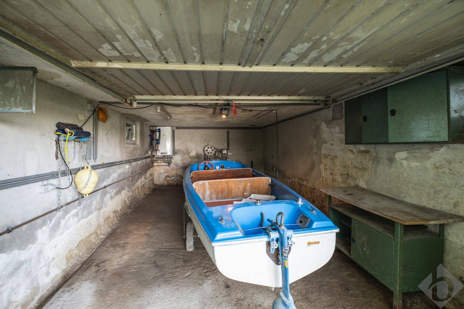 Einfache Bootsgarage mit Betonboden und einem blauen Boot auf einem Anhänger.