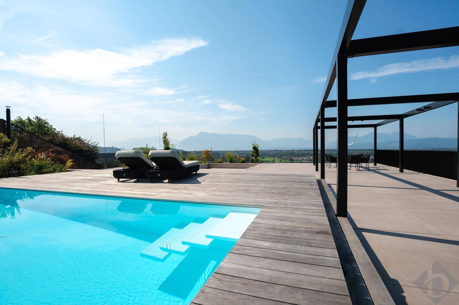 Großzügige Poollandschaft mit Holzdeck, Pergola und atemberaubendem Blick auf die Bergwelt.