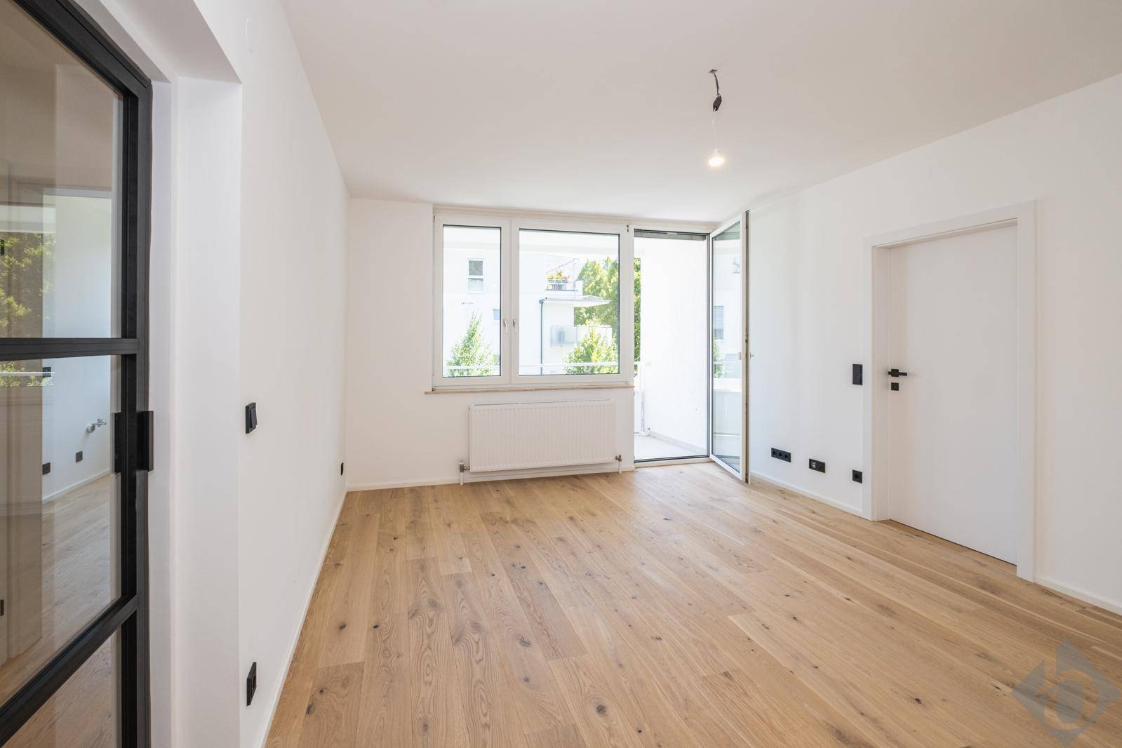 Heller Wohnraum mit Eichenparkett, großen Fenstern und Zugang zu einem Balkon.