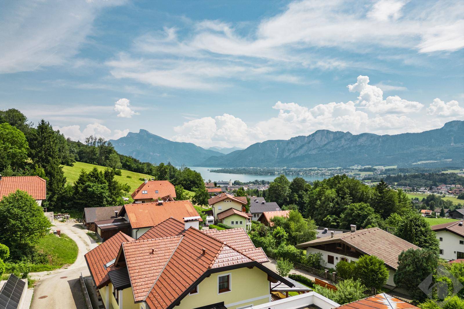 Malerischer Ausblick auf ein Dorf, einen See und die umliegende Berglandschaft unter blauem Himmel.