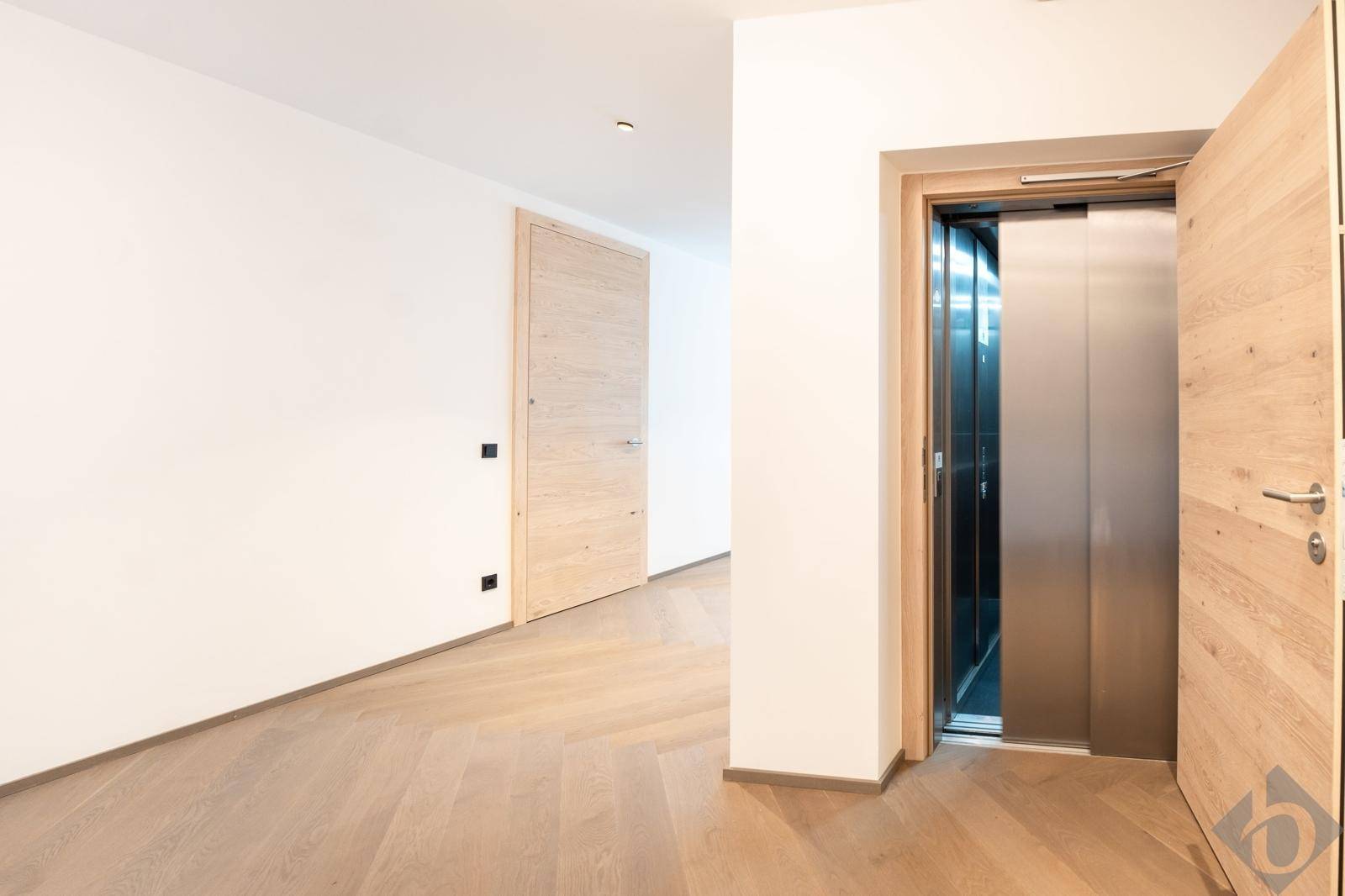 Heller Flur mit Holzboden und direktem Zugang zu einem modernen Aufzug im Gebäude.