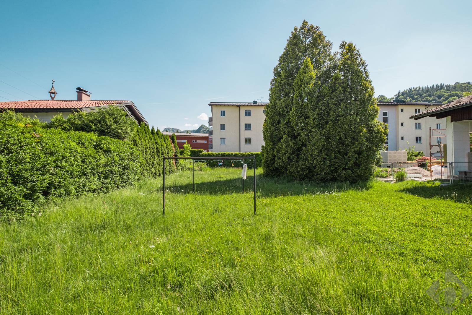 Grüner Gartenbereich mit Wäscheleine und hohen Hecken, im Hintergrund Mehrfamilienhäuser.